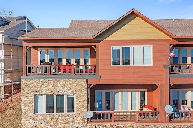 rear view of property with stone siding, a shingled roof, and a balcony