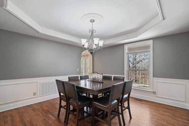 dining space with arched walkways, a raised ceiling, visible vents, and wood finished floors