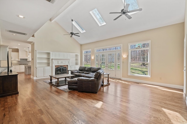 living room with beam ceiling, visible vents, a ceiling fan, a brick fireplace, and wood finished floors