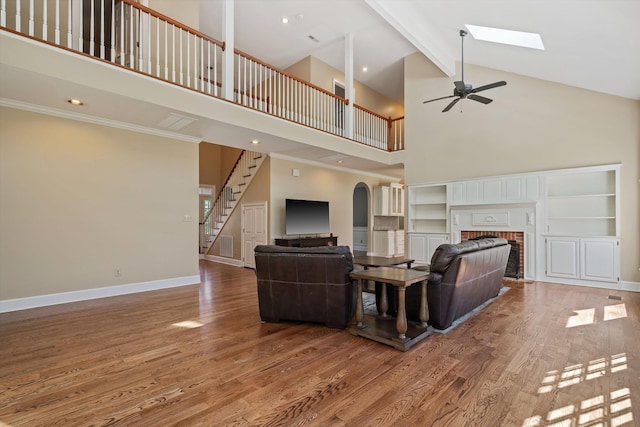 living room with wood finished floors, baseboards, stairs, a brick fireplace, and beam ceiling