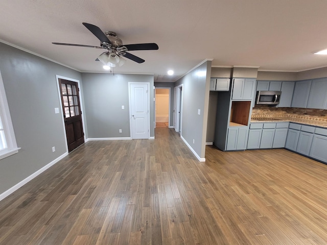 kitchen with gray cabinetry, wood finished floors, ornamental molding, decorative backsplash, and stainless steel microwave