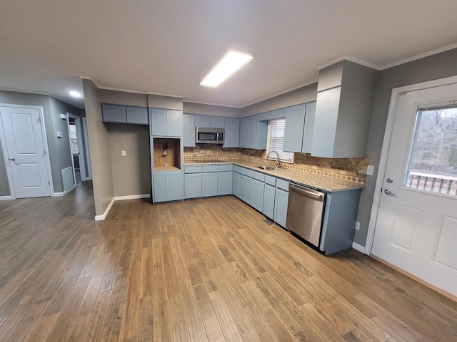 kitchen featuring crown molding, stainless steel appliances, tasteful backsplash, light wood-style flooring, and a sink