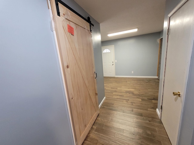 hall with a barn door, wood finished floors, and baseboards