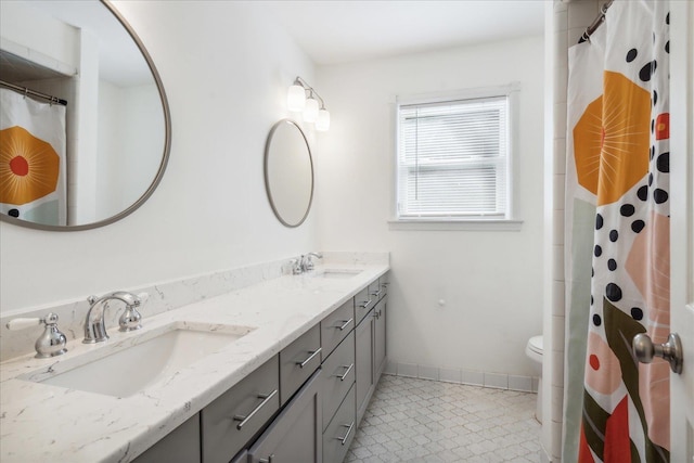 full bath with double vanity, baseboards, toilet, and a sink