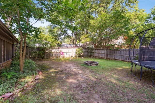 view of yard with a fenced backyard, a trampoline, and a fire pit