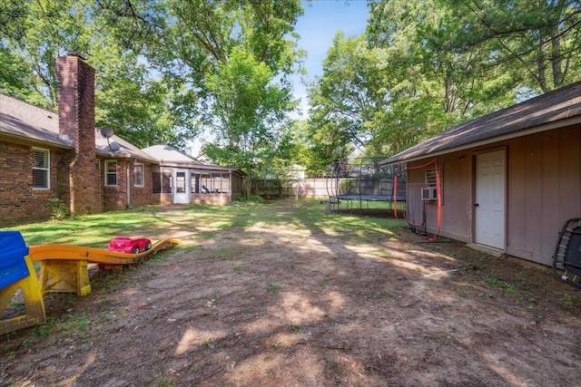 view of yard featuring a trampoline, a sunroom, fence, and an outdoor structure