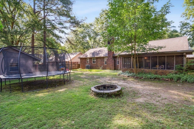 view of yard featuring a trampoline, a sunroom, fence, and a fire pit