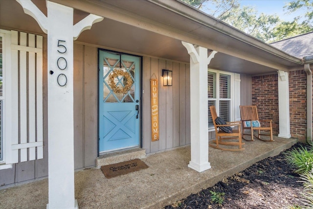 entrance to property with roof with shingles, a porch, board and batten siding, and brick siding