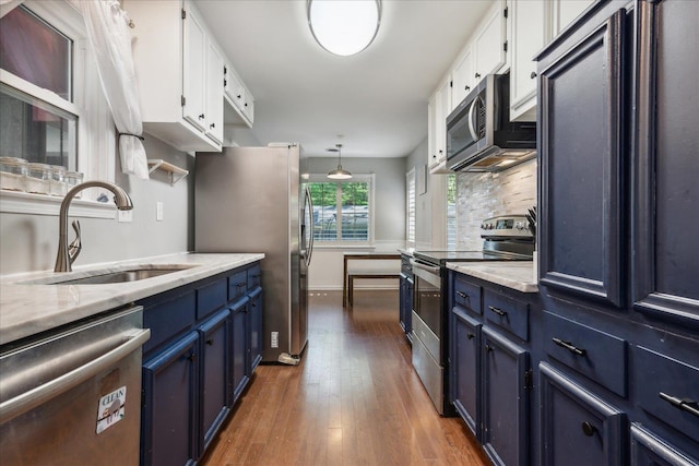 kitchen with blue cabinets, stainless steel appliances, wood finished floors, a sink, and white cabinetry