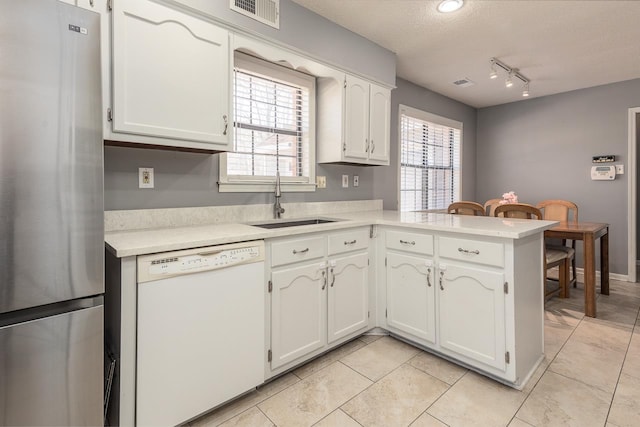 kitchen featuring visible vents, white cabinets, freestanding refrigerator, white dishwasher, and a sink