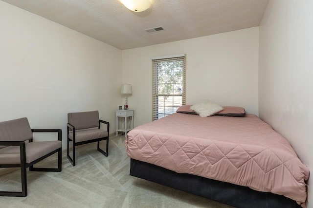 bedroom featuring light carpet, visible vents, and a textured ceiling