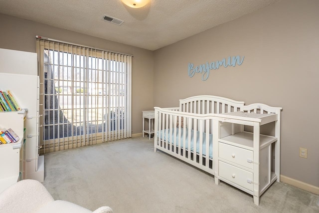 carpeted bedroom with a crib, baseboards, visible vents, and a textured ceiling