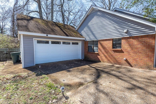 view of property exterior featuring brick siding, roof with shingles, fence, a garage, and driveway