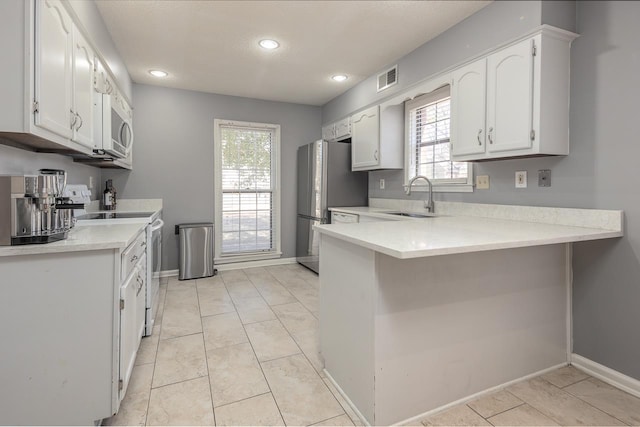 kitchen featuring light countertops, electric range, white cabinets, a sink, and a peninsula