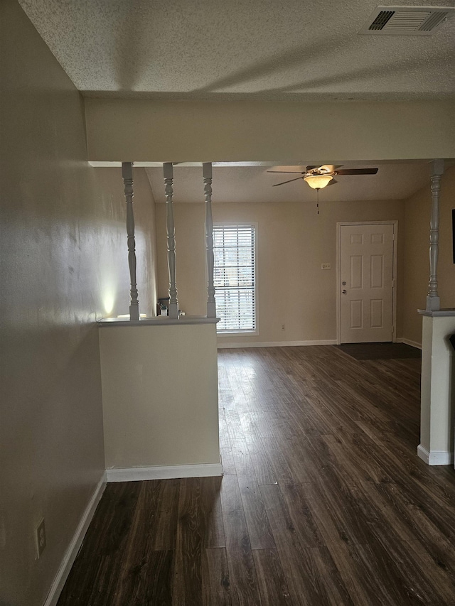 unfurnished living room featuring dark wood-style flooring, visible vents, a ceiling fan, a textured ceiling, and baseboards