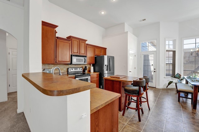 kitchen featuring arched walkways, a breakfast bar, visible vents, appliances with stainless steel finishes, and tasteful backsplash