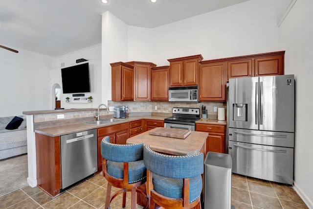 kitchen with brown cabinetry, tile patterned flooring, stainless steel appliances, light countertops, and a sink