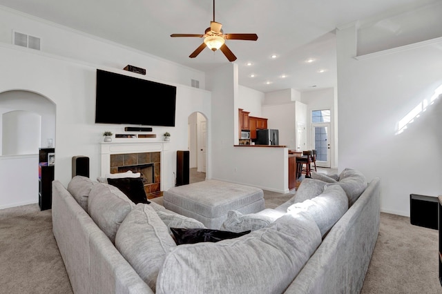 living area with arched walkways, visible vents, light carpet, a tile fireplace, and baseboards