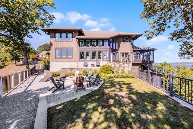 back of house with a fire pit, fence, stone siding, a lawn, and a patio area