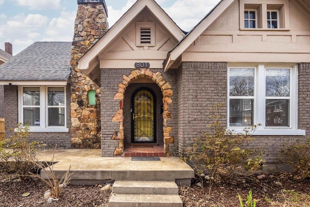 property entrance with a shingled roof, a chimney, and brick siding