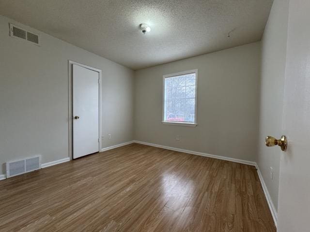 unfurnished room featuring a textured ceiling, wood finished floors, visible vents, and baseboards