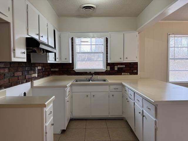 kitchen featuring visible vents, a sink, a textured ceiling, a peninsula, and under cabinet range hood