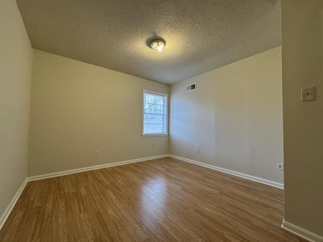 empty room with visible vents, a textured ceiling, baseboards, and wood finished floors