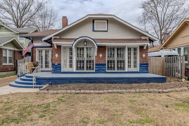 rear view of property with french doors, brick siding, fence, and a chimney