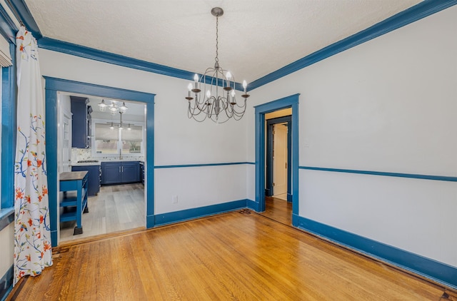 empty room with a textured ceiling, a notable chandelier, baseboards, light wood finished floors, and crown molding