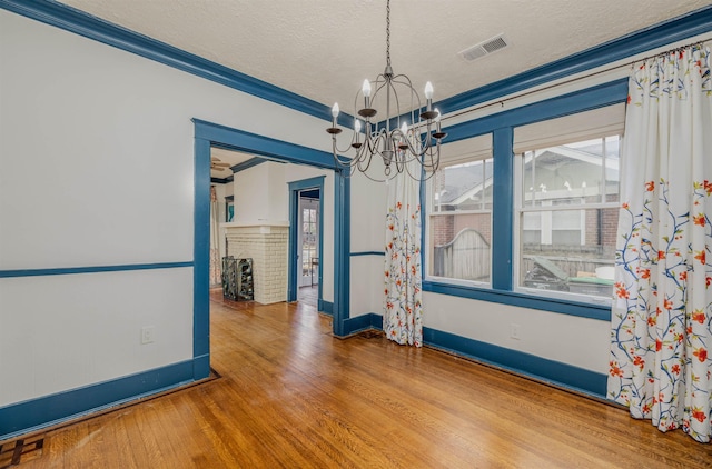 empty room featuring visible vents, wood finished floors, an inviting chandelier, a textured ceiling, and a brick fireplace