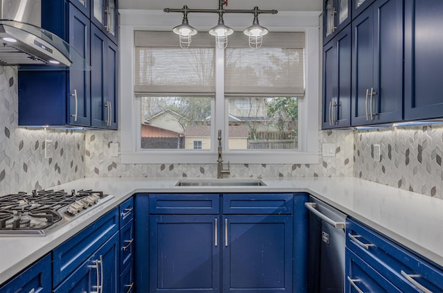 kitchen featuring wall chimney range hood, appliances with stainless steel finishes, blue cabinetry, and a sink