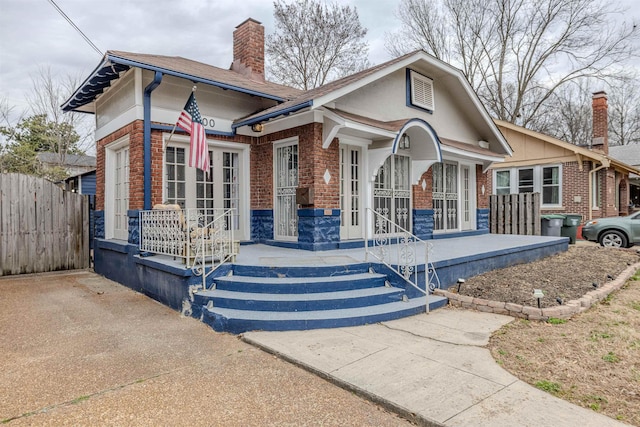 bungalow-style house with covered porch, brick siding, fence, and a chimney