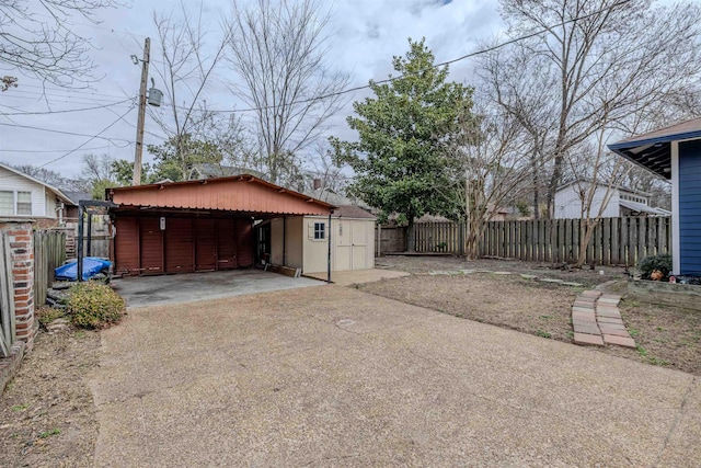 garage with a carport, a storage unit, fence, and concrete driveway