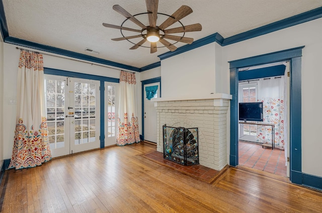 unfurnished living room with french doors, wood-type flooring, ornamental molding, a brick fireplace, and a textured ceiling