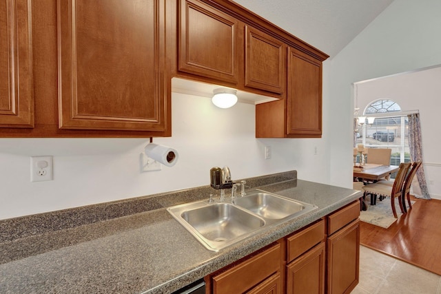 kitchen with light wood-style flooring, a sink, vaulted ceiling, brown cabinetry, and dark countertops