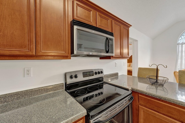 kitchen featuring lofted ceiling, stainless steel appliances, stone countertops, and brown cabinets