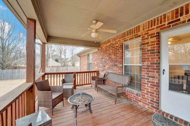 wooden terrace featuring ceiling fan, fence, and an outdoor living space with a fire pit