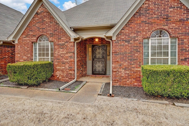 entrance to property featuring a shingled roof and brick siding