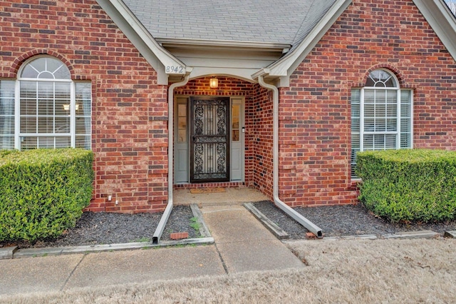 doorway to property featuring a shingled roof and brick siding