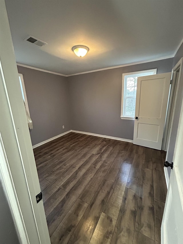 empty room with ornamental molding, visible vents, dark wood finished floors, and baseboards