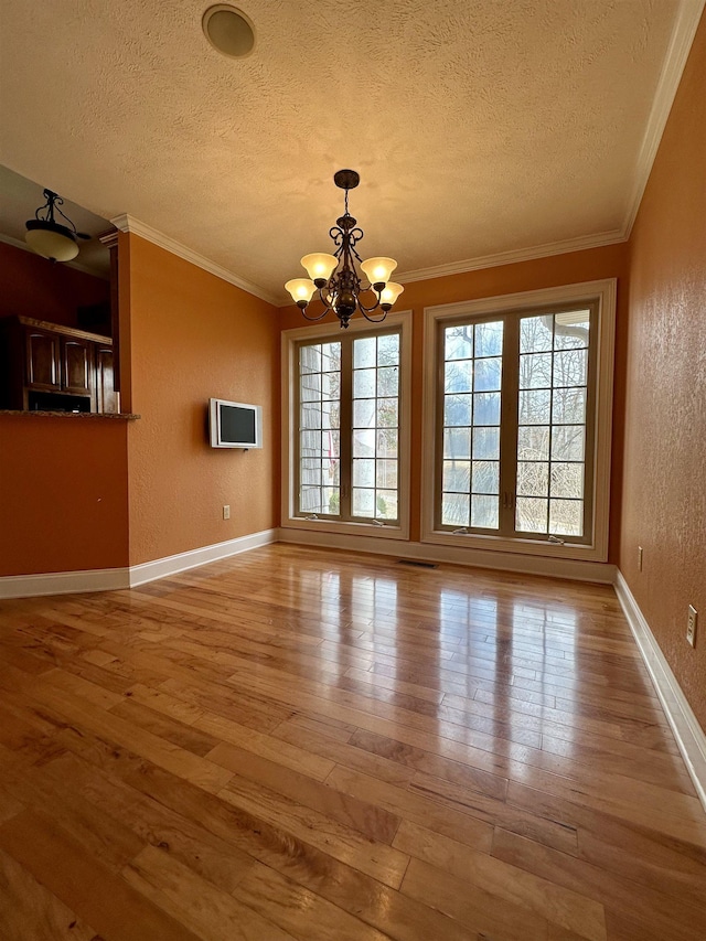 unfurnished dining area featuring a textured ceiling, a textured wall, hardwood / wood-style flooring, a notable chandelier, and crown molding