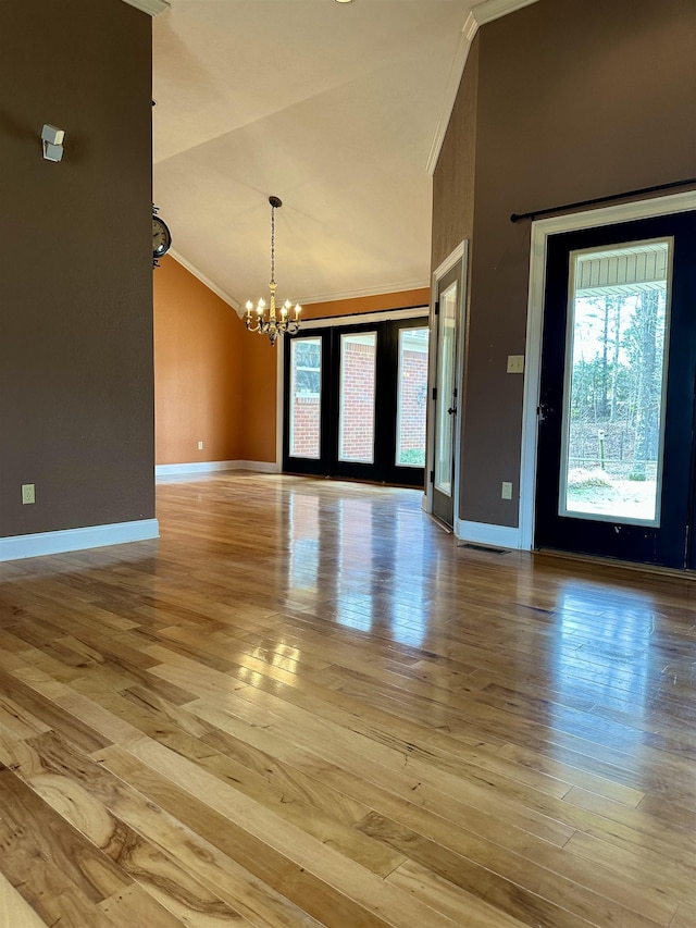 empty room with a chandelier, ornamental molding, wood finished floors, and baseboards