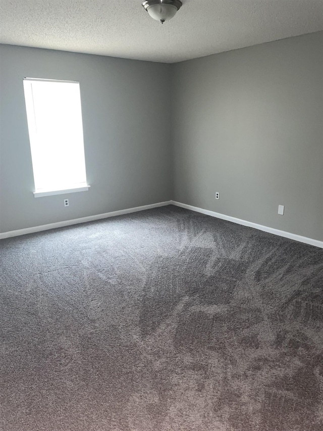 unfurnished room with a textured ceiling, dark carpet, and baseboards