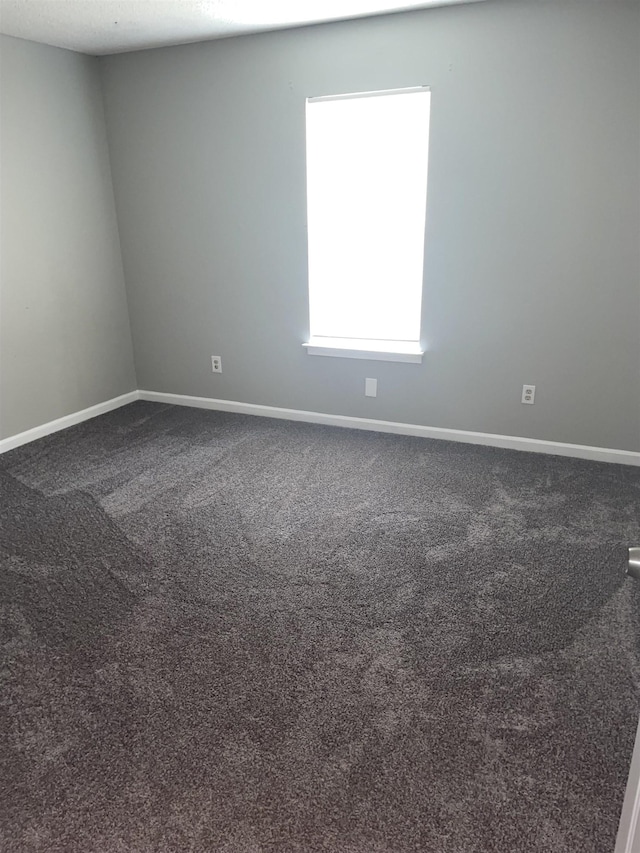 spare room featuring dark colored carpet and baseboards