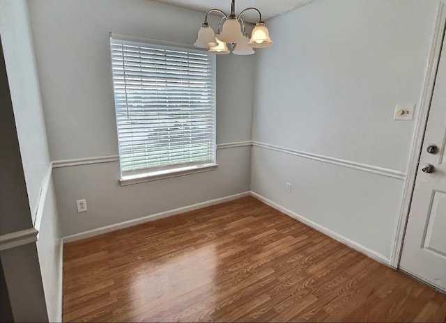 unfurnished dining area with baseboards, a notable chandelier, and wood finished floors