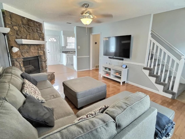 living room with a fireplace, stairway, a ceiling fan, wood finished floors, and baseboards