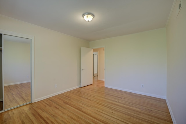 unfurnished bedroom featuring visible vents, baseboards, ornamental molding, light wood-style floors, and a closet