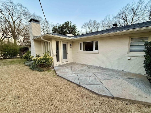 rear view of property featuring a yard, brick siding, a chimney, and a patio area