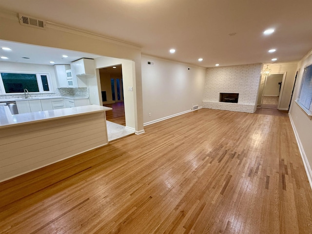 unfurnished living room with a brick fireplace, light wood-style floors, visible vents, and ornamental molding