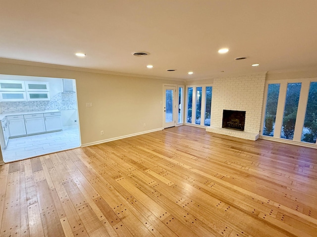 unfurnished living room with recessed lighting, visible vents, ornamental molding, light wood-type flooring, and a brick fireplace